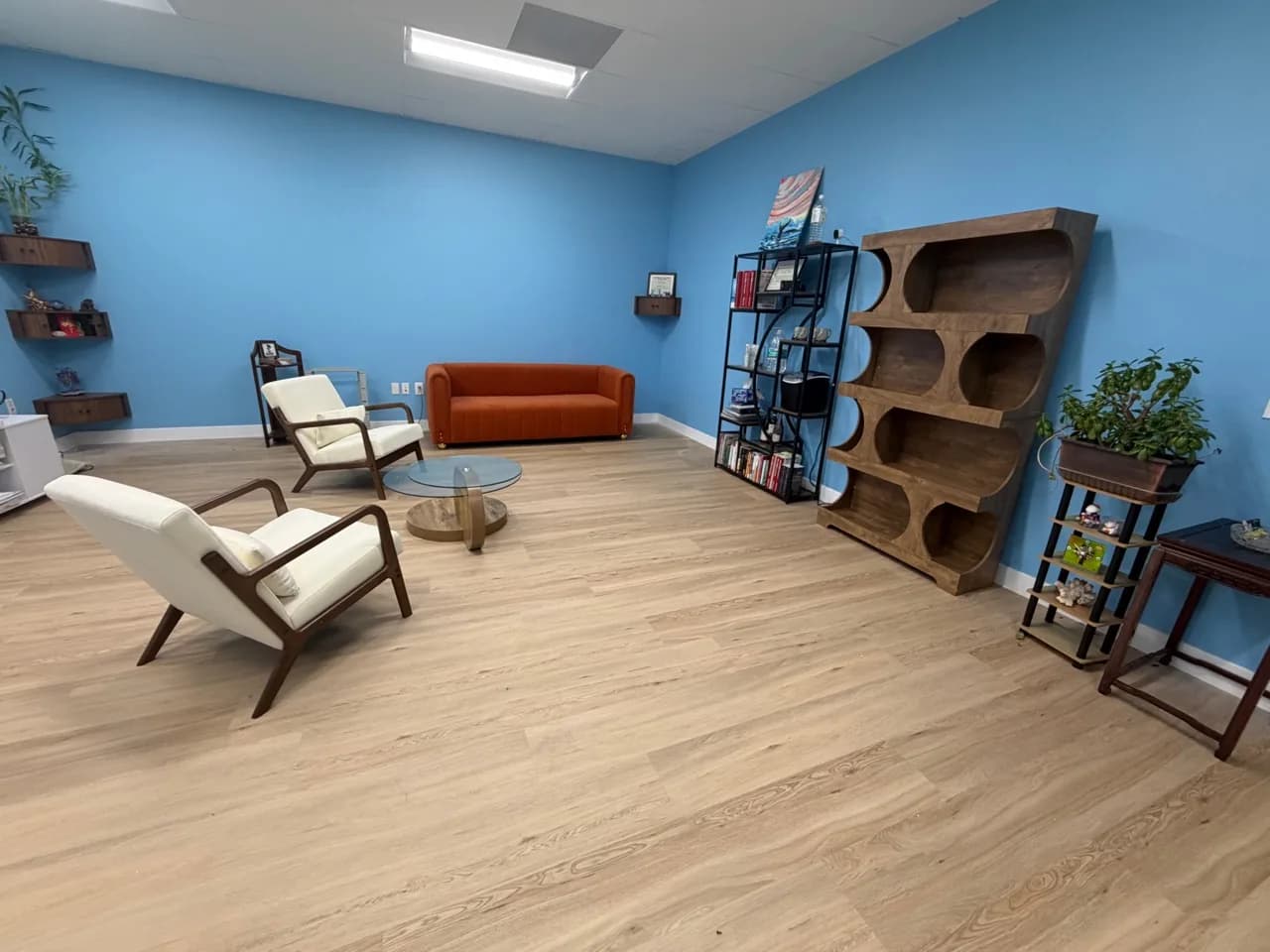 A finished living-room furniture arrangement with a sofa, two accent chairs, a round coffee table, and a tall wood display shelf, fully assembled and in place.