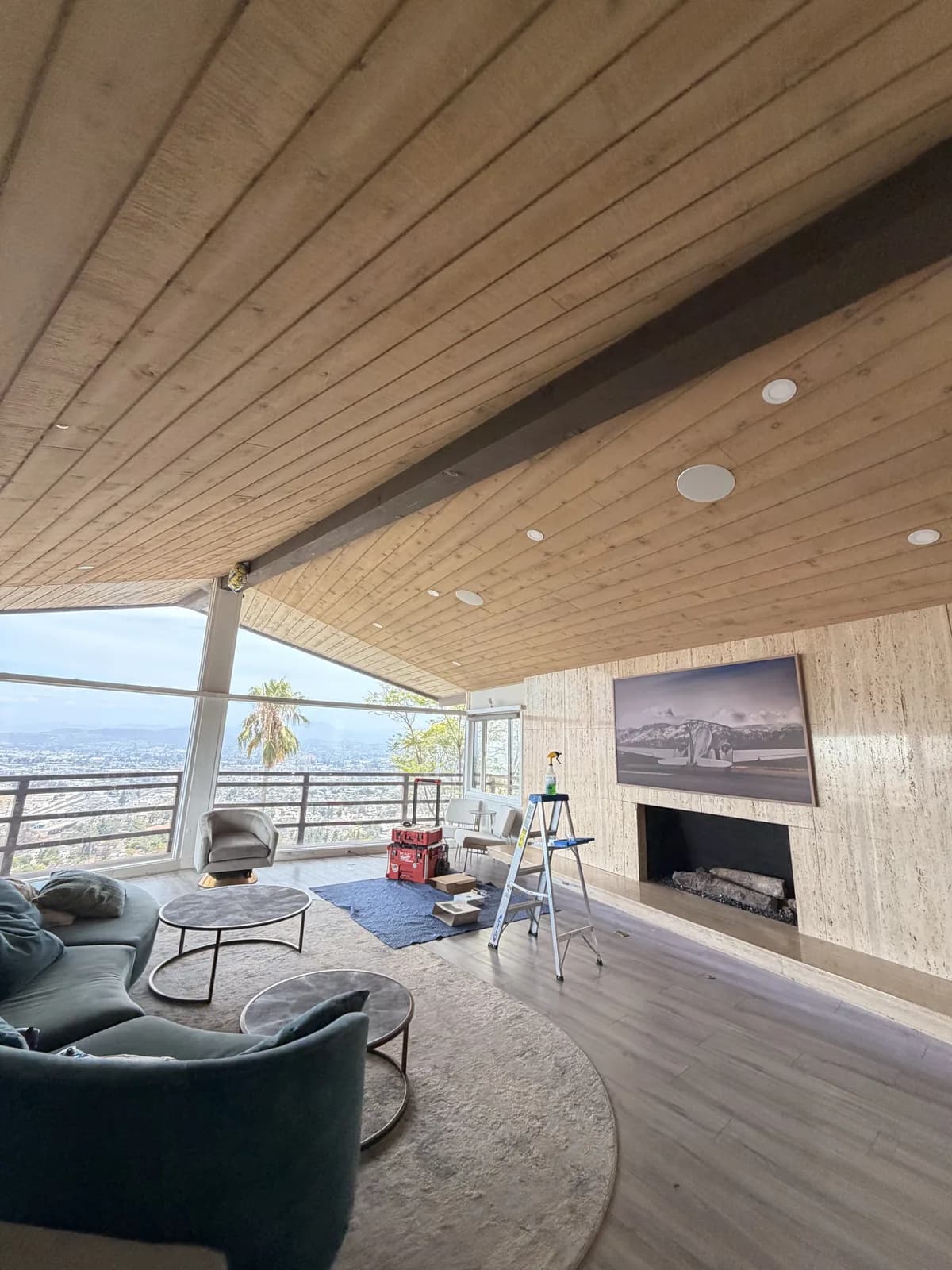 A finished media room with a wall-mounted display above a stone fireplace and recessed ceiling speakers built into a wood-plank vaulted ceiling.