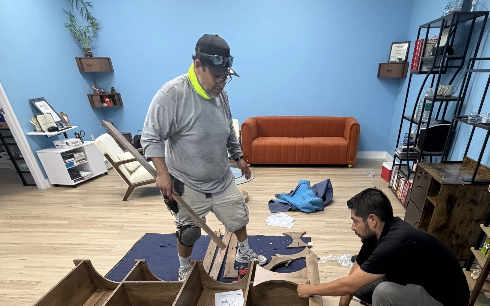 Two installers coordinating the assembly of a large wood furniture piece in an office.