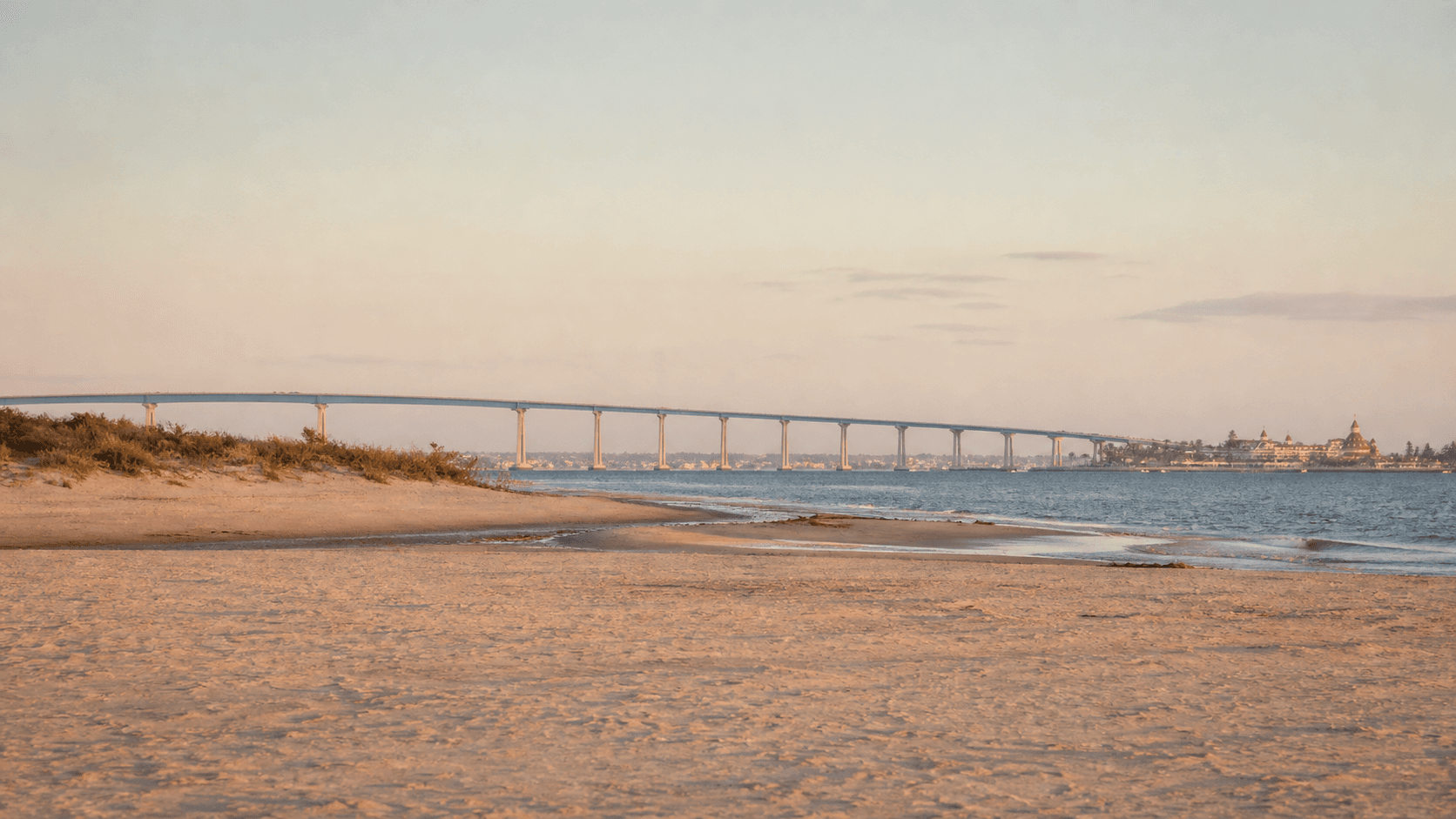Illustrative golden Coronado beach with a distant bay bridge and Victorian landmark silhouette.