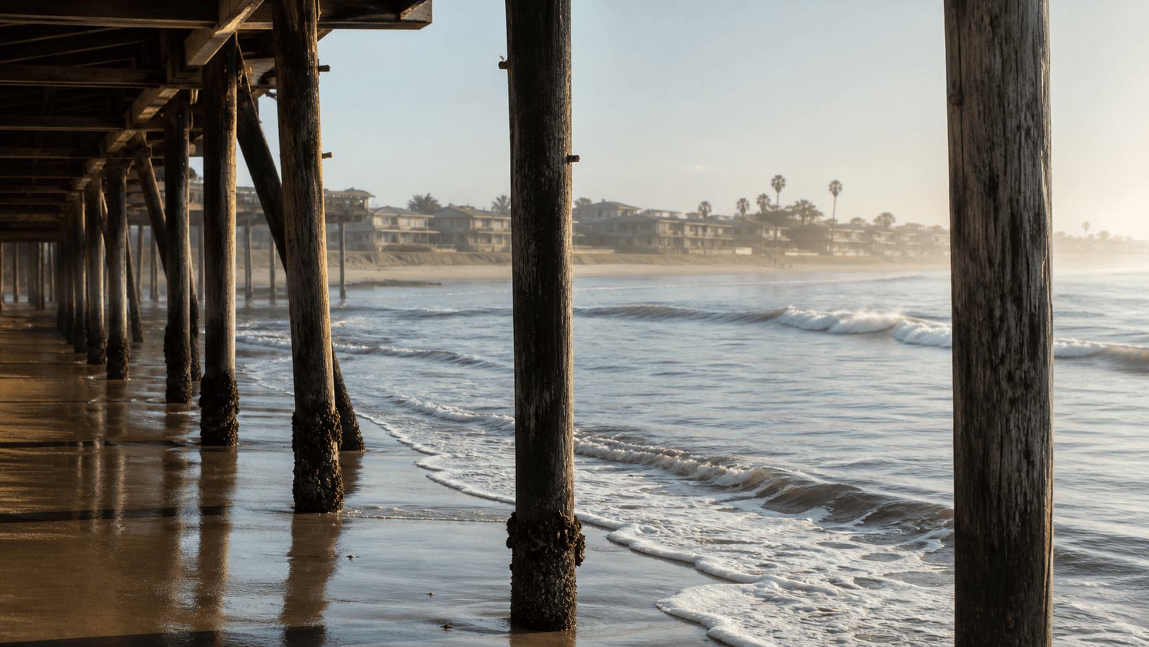 Illustrative view through pier pilings and surf inspired by Pacific Beach.